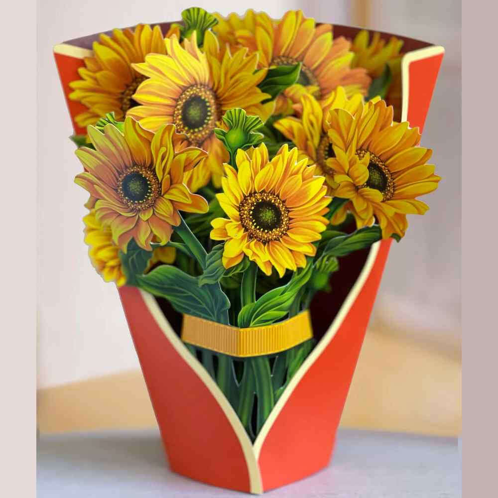 image of paper bouquet opened, with a red orange wrap and bright yellow sunflower blooms with a yellow ribbon around the stems