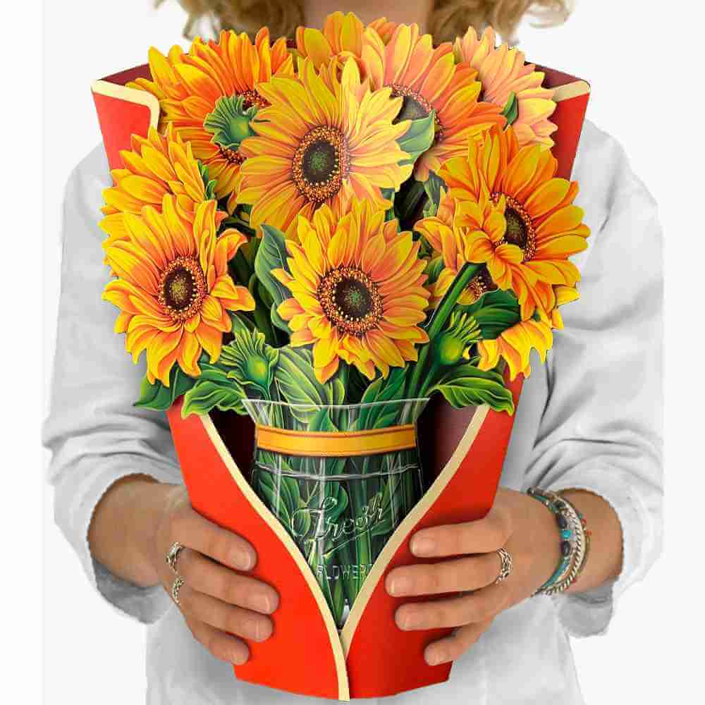 image of paper bouquet opened, with a red orange wrap and bright yellow sunflower blooms with a yellow ribbon around the stems