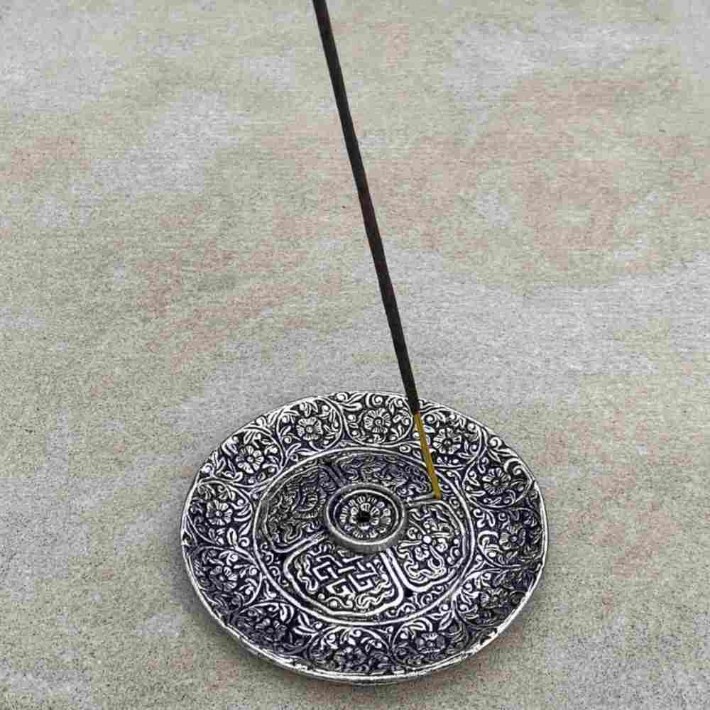closeup image of round, intricately detailed tray, with an incense stick standing in tray